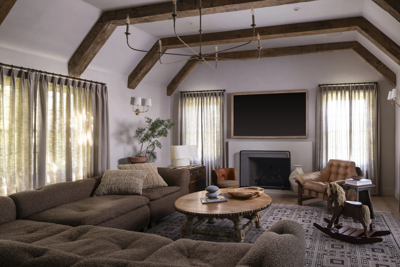 Living room with exposed timber beams, a fireplace, and curved seating at Adobe Canyon Farmhouse