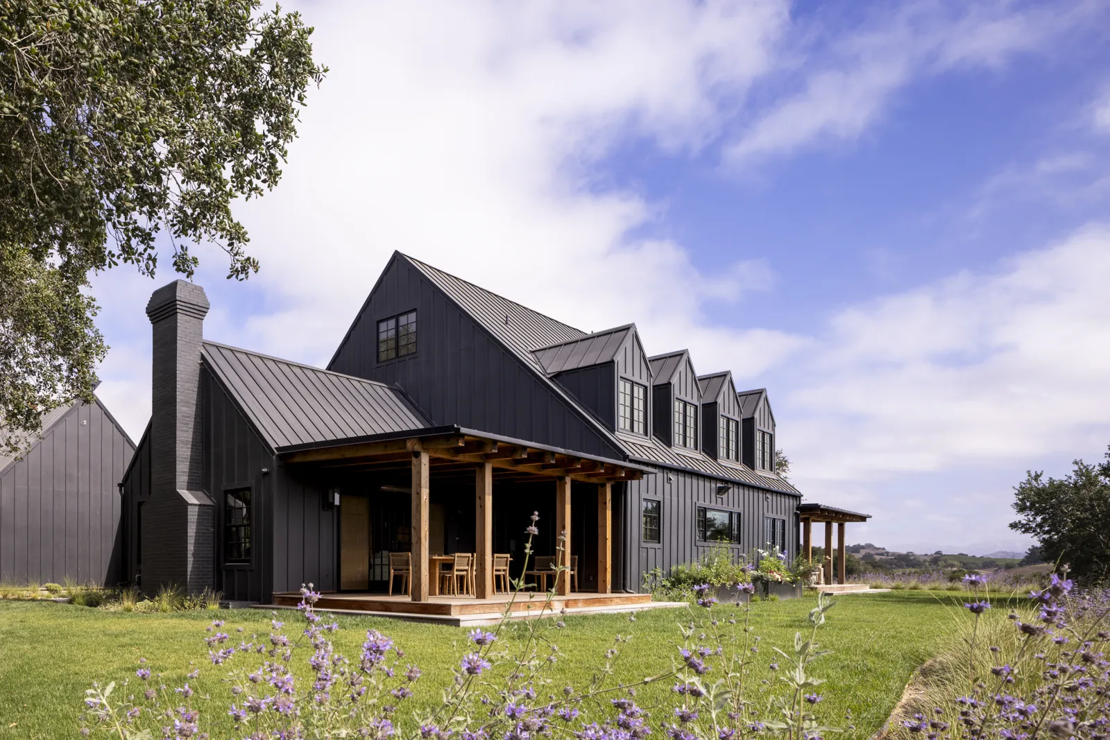 Adobe Canyon Farmhouse in Solvang with dark siding, a metal roof, dormer windows, and a timber-covered porch