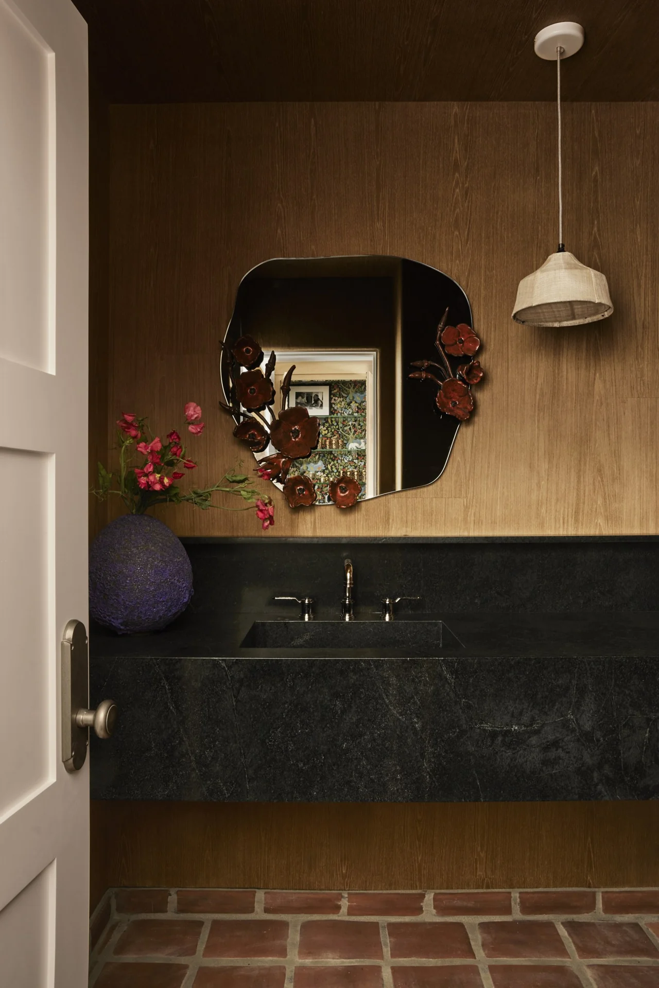 Powder room with dark stone vanity and floral mirror