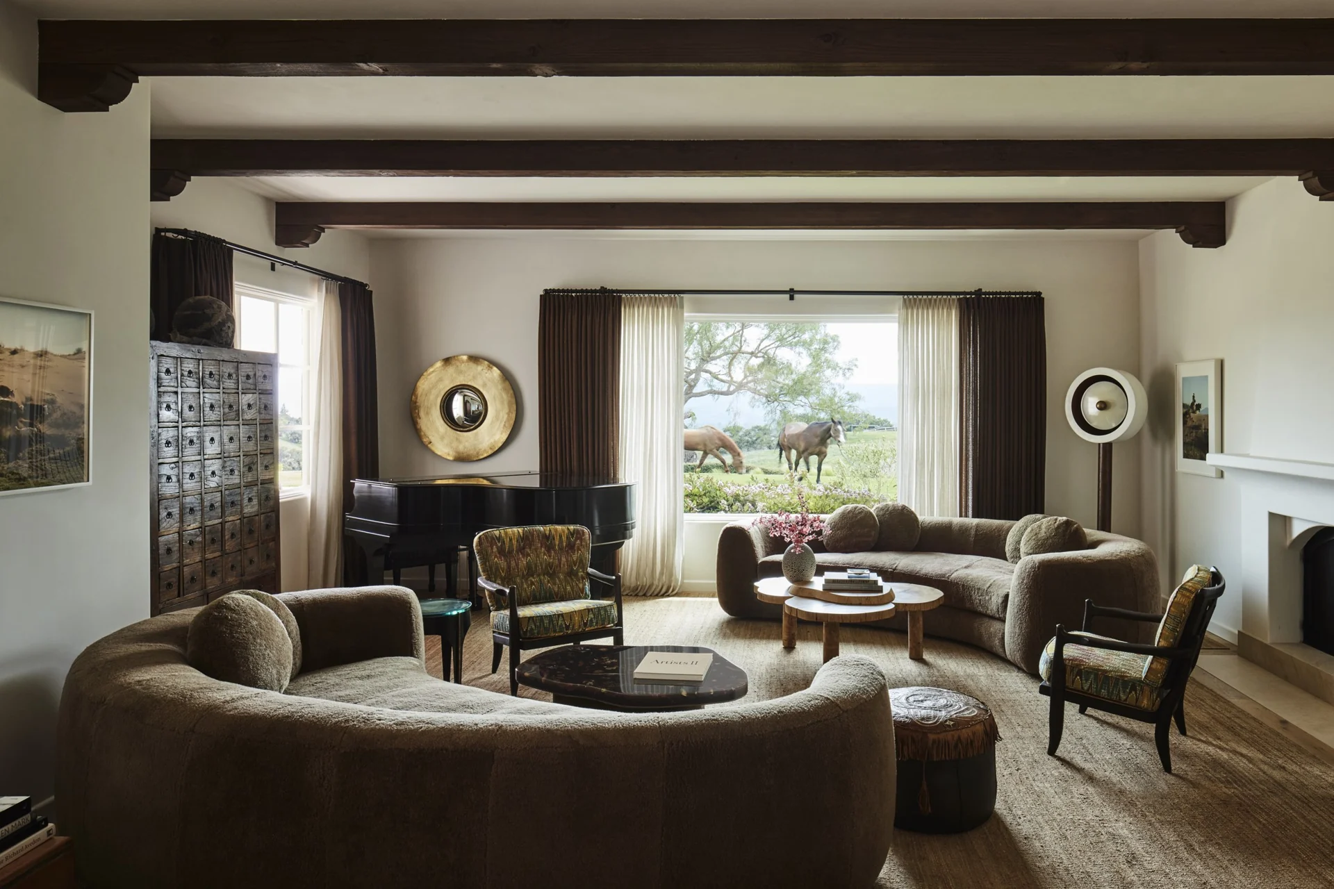 Living room with curved sofas, a grand piano, and views of horses in the landscape